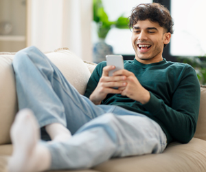 Happy Middle Eastern Young Man Using Cellphone Laughing At Home